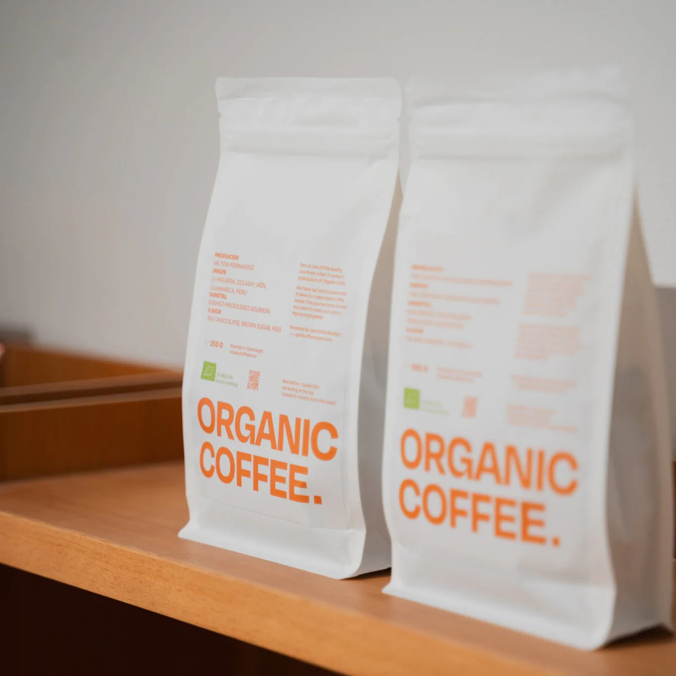 Două pungi de cafea boabe April Organic Coffee expuse pe un raft de lemn în shop de cafea de specialitate.