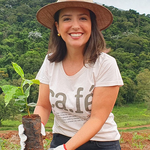 Coffee Community farmer Carolina Alckmin wearing a straw hat and holding a young coffee plant at Santo Antonio farm.