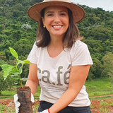 Coffee Community farmer Carolina Alckmin wearing a straw hat and holding a young coffee plant at Santo Antonio farm.