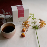 Coffee Community Columbia Alto Naranjal coffee box with a ceramic cup of brewed coffee and fresh tiger lilies