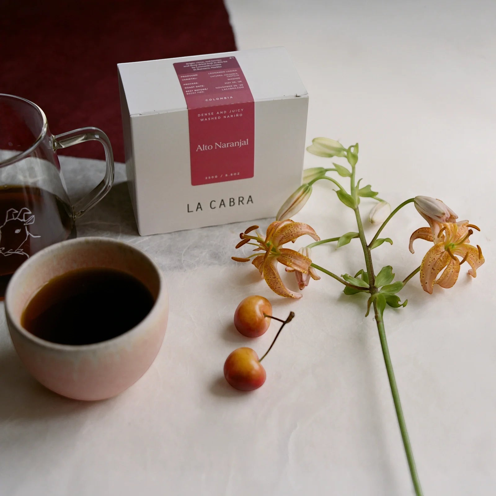 Coffee Community Columbia Alto Naranjal coffee box with a ceramic cup of brewed coffee and fresh tiger lilies
